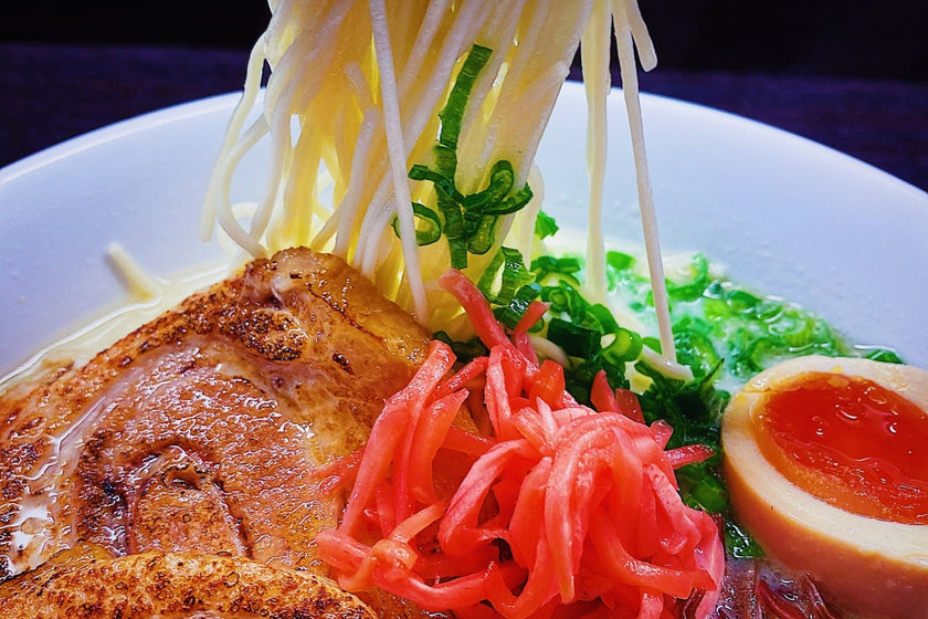 a lift of thin hakata noodles out of a bowl of tonkotsu